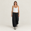 A woman modeling a pair of loose black wide-leg hiking pants with a adjustable waist, paired with a white ribbed camisole top and gray sneakers, against a plain off-white studio background.