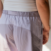 Close-up of a person wearing lilac hiking pants with a small 'be there' logo on the left hip, paired with a white tank top.